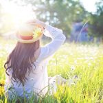 Garota com chapéu de palha e vestido branco, andando em um campo de flores. Sol ao fundo