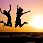 duas mulheres pulando alto na praia ao pôr do sol