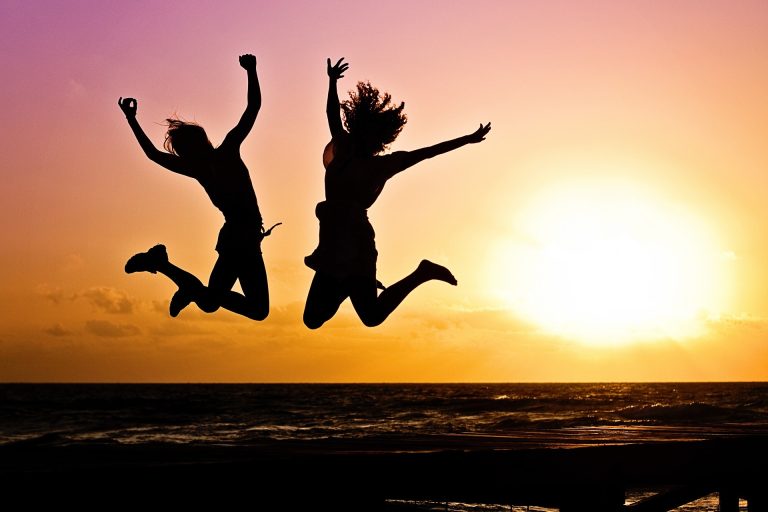 duas mulheres pulando alto na praia ao pôr do sol