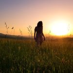 mulher de vestido, andando em campo em direção a um por de sol