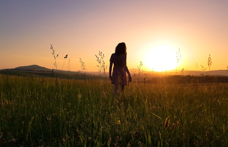 mulher de vestido, andando em campo em direção a um por de sol