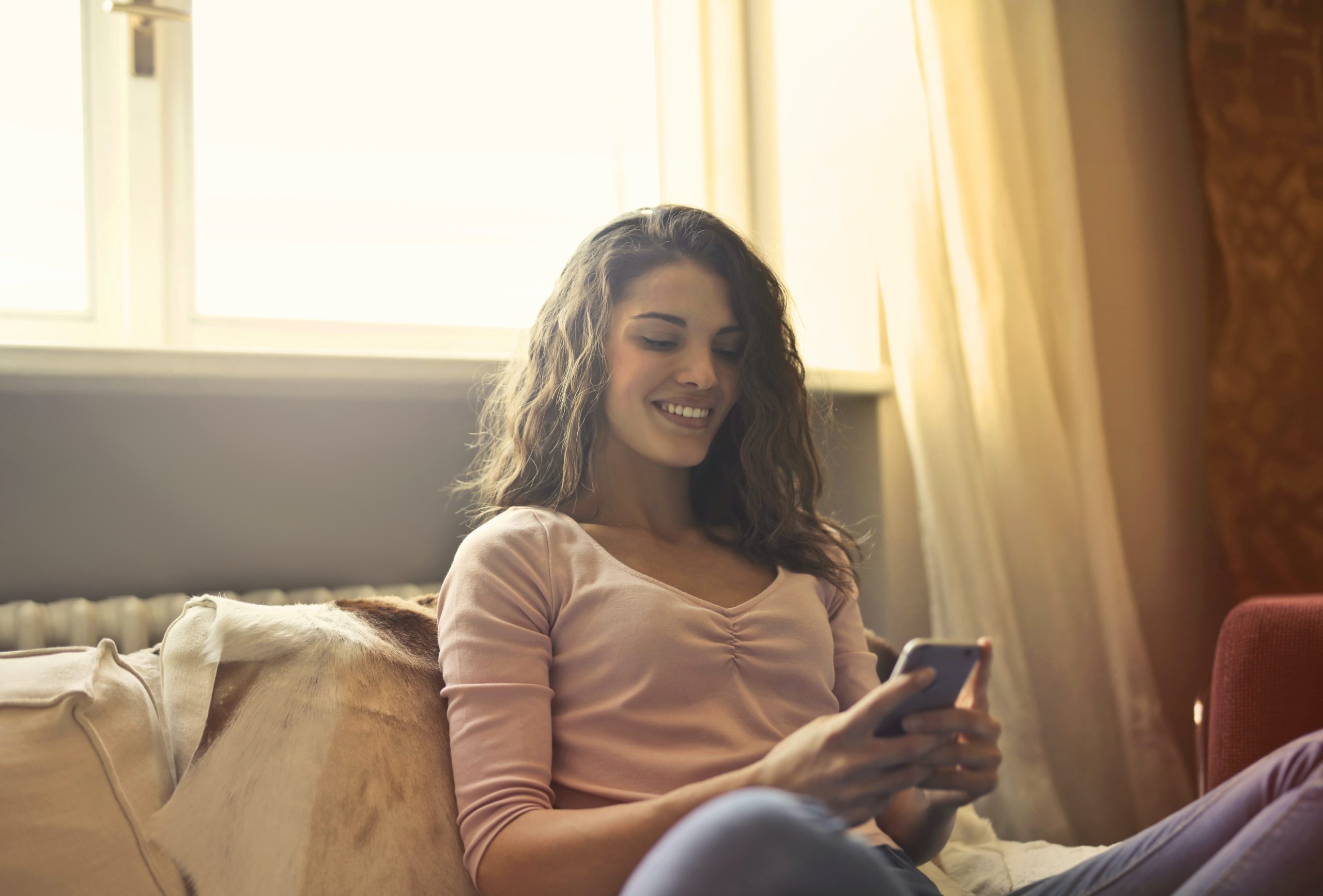 Mulher sentada na cama, olhando o celular