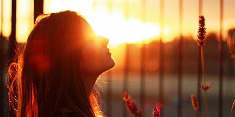 Moça de olhos fechados, grade e sol poente ao fundo