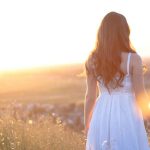 mulher de vestido branco, andando em campo de flores, com sol ao fundo