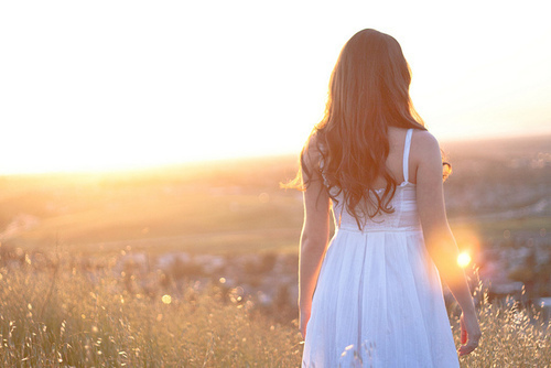 mulher de vestido branco, andando em campo de flores, com sol ao fundo